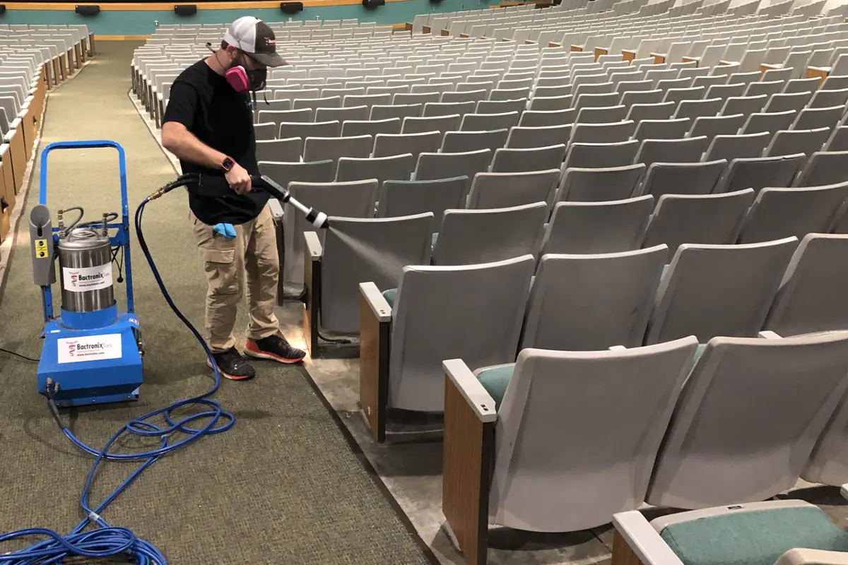 A Bactronix technician applying treatment with the company's electrostatic sprayer along rows of seating in a large auditorium